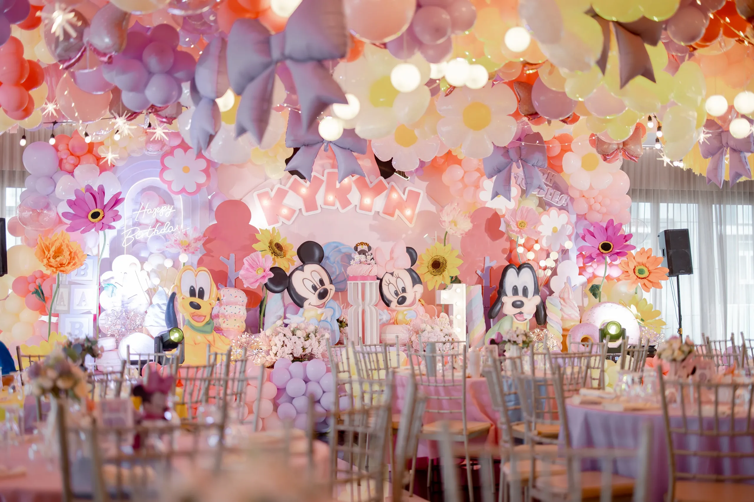 Minnie Mouse birthday backdrop for Kyryn with oversized daisies, pastel balloons, bows and Disney character decorations