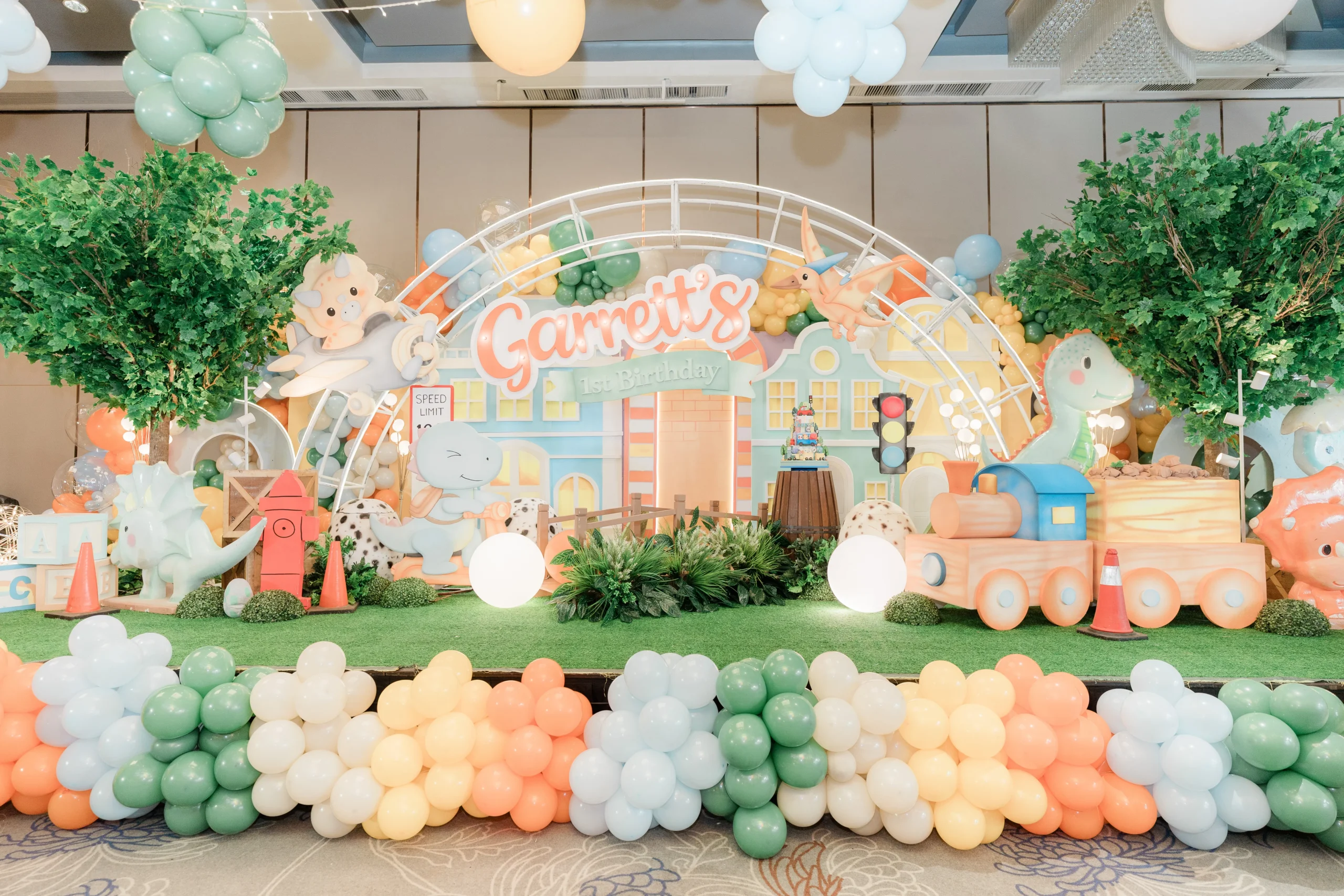 Pastel dinosaur birthday stage with balloons, trees and city decorations
