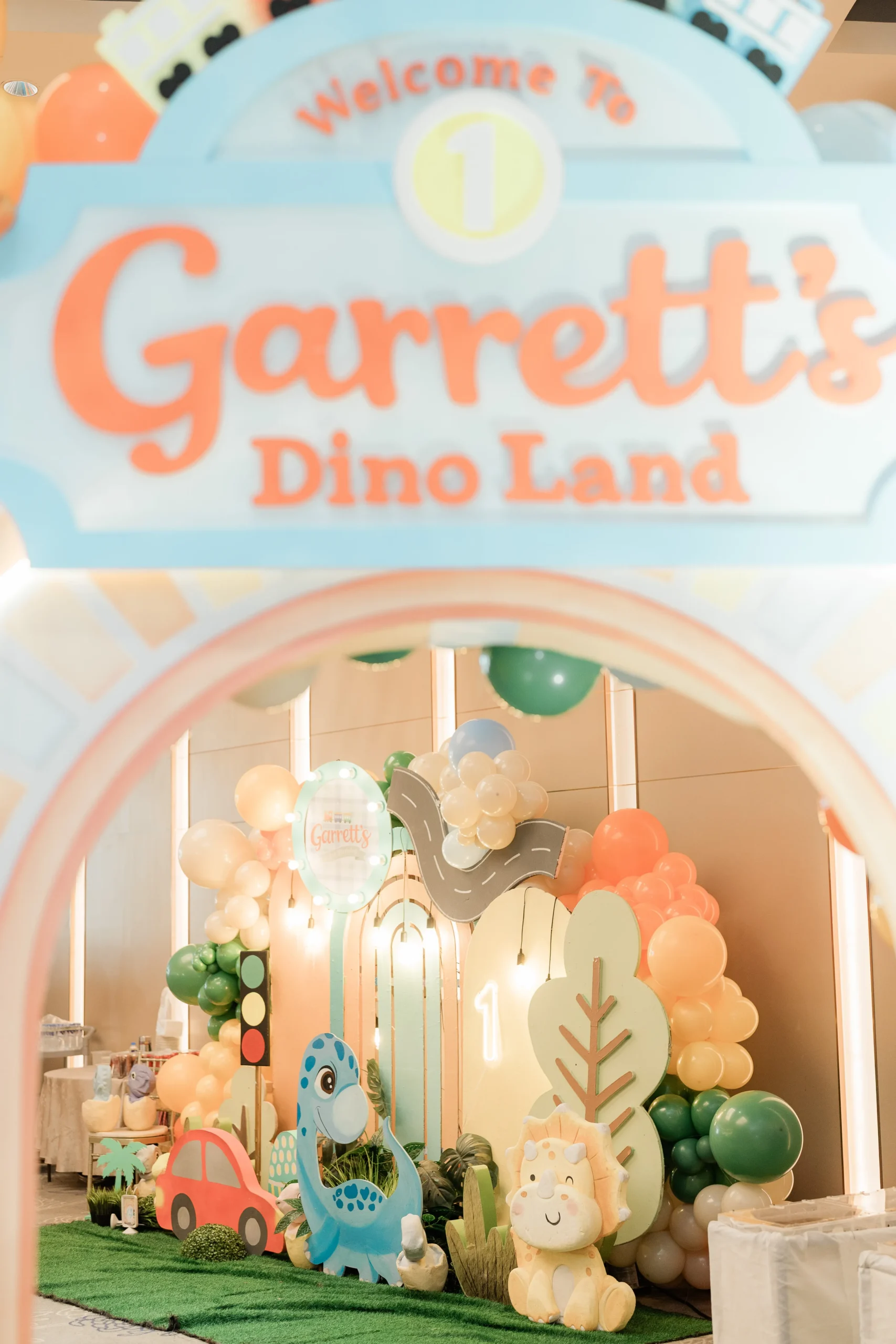 Pastel dinosaur birthday stage with balloons, trees and city decorations