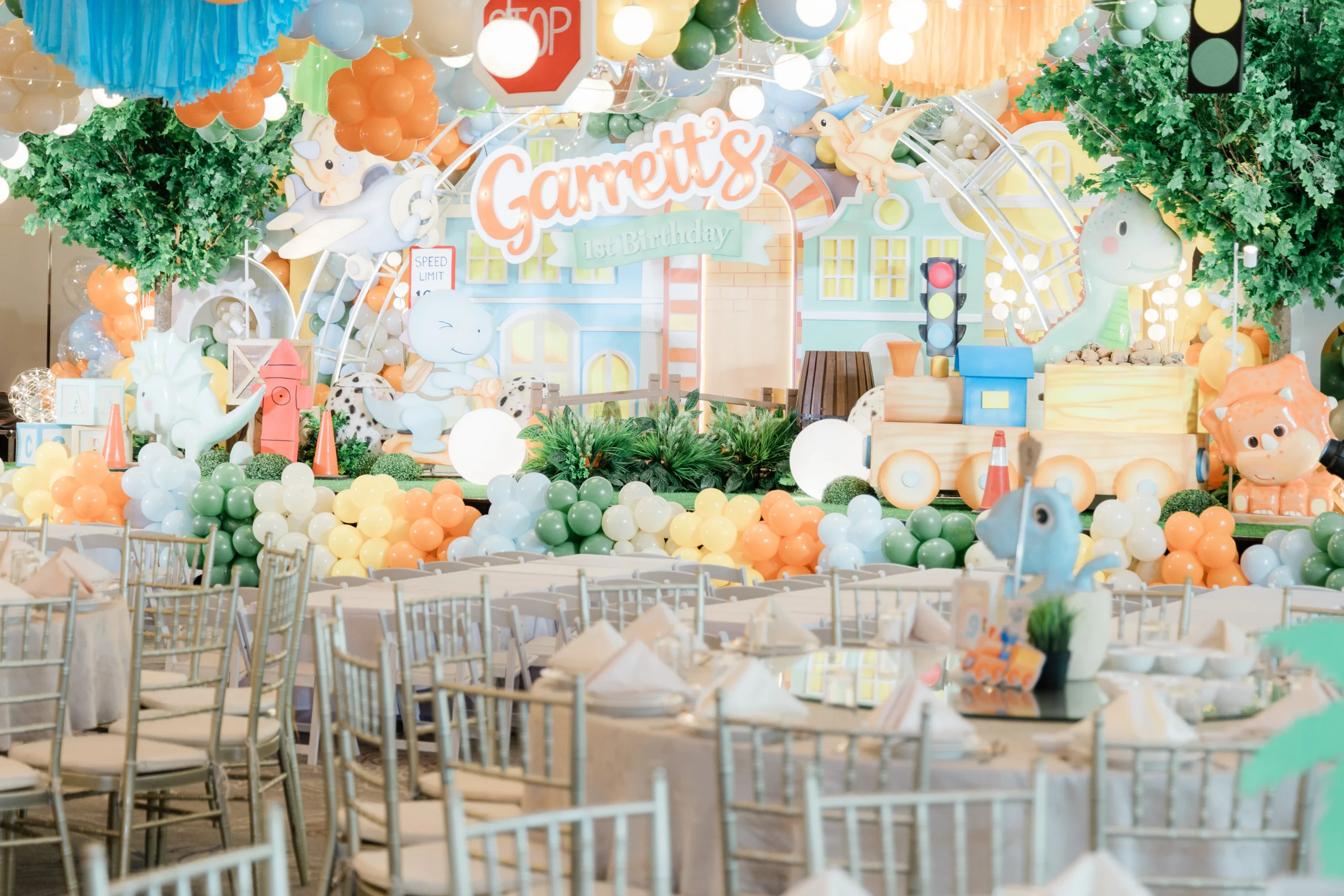 Pastel dinosaur birthday stage with balloons, trees and city decorations