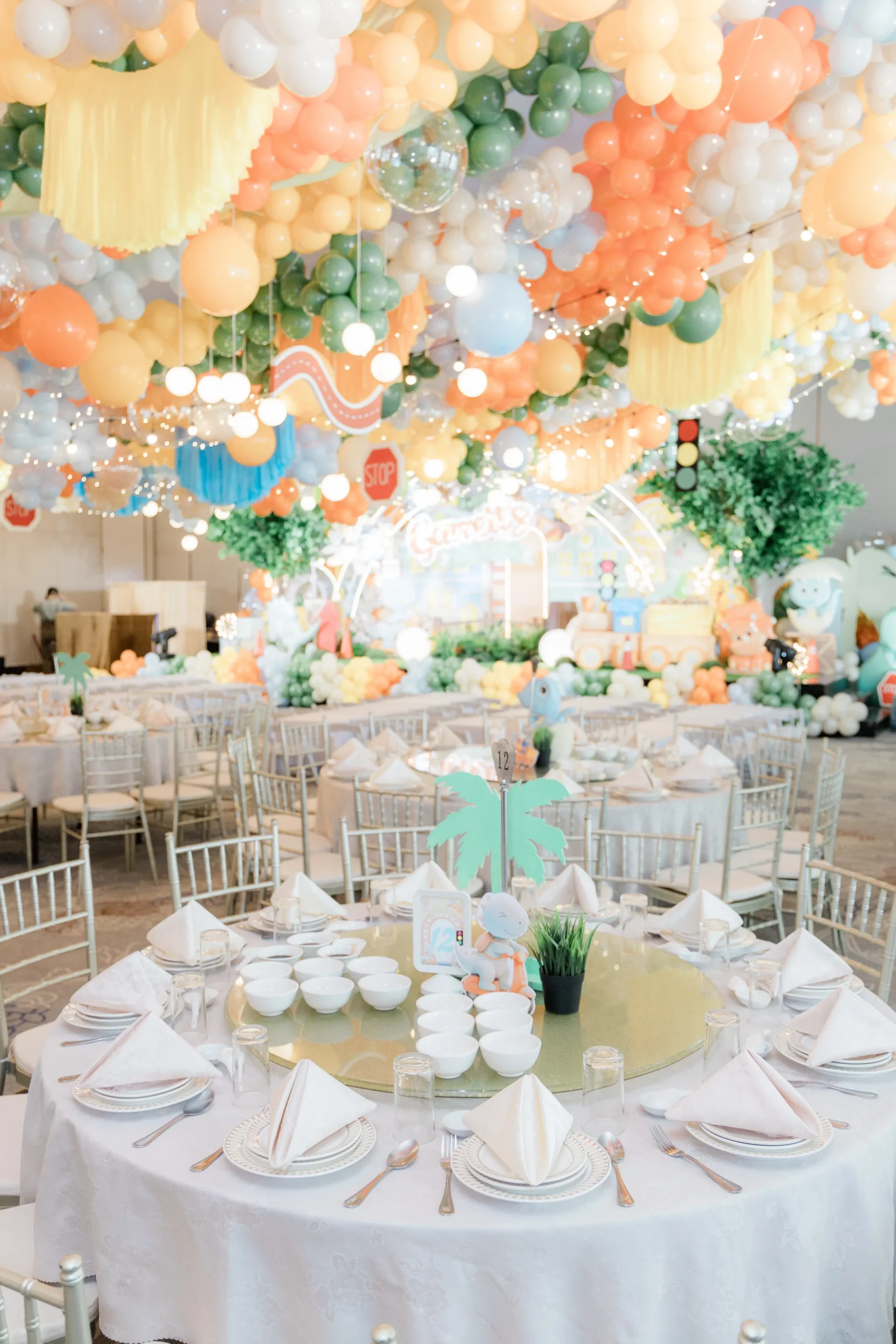 Pastel dinosaur birthday stage with balloons, trees and city decorations