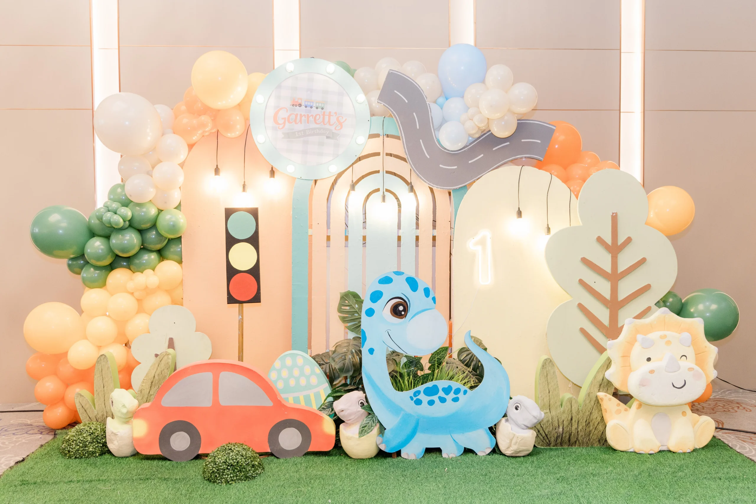 Pastel dinosaur birthday stage with balloons, trees and city decorations