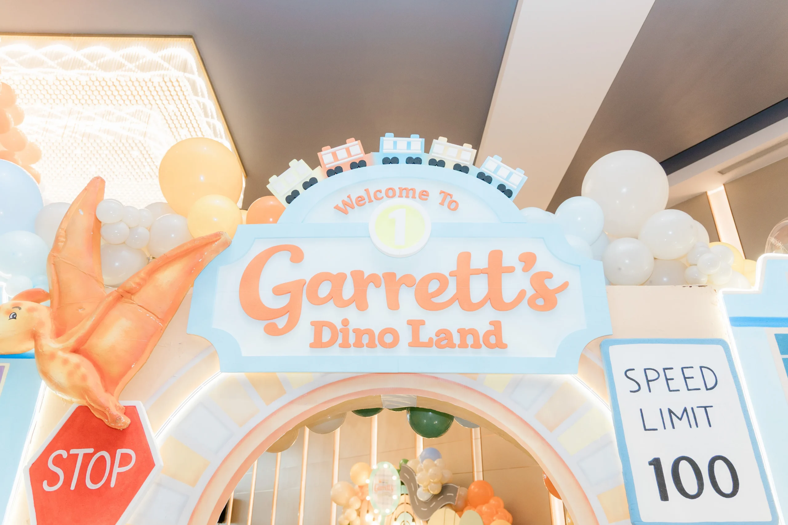 Pastel dinosaur birthday stage with balloons, trees and city decorations