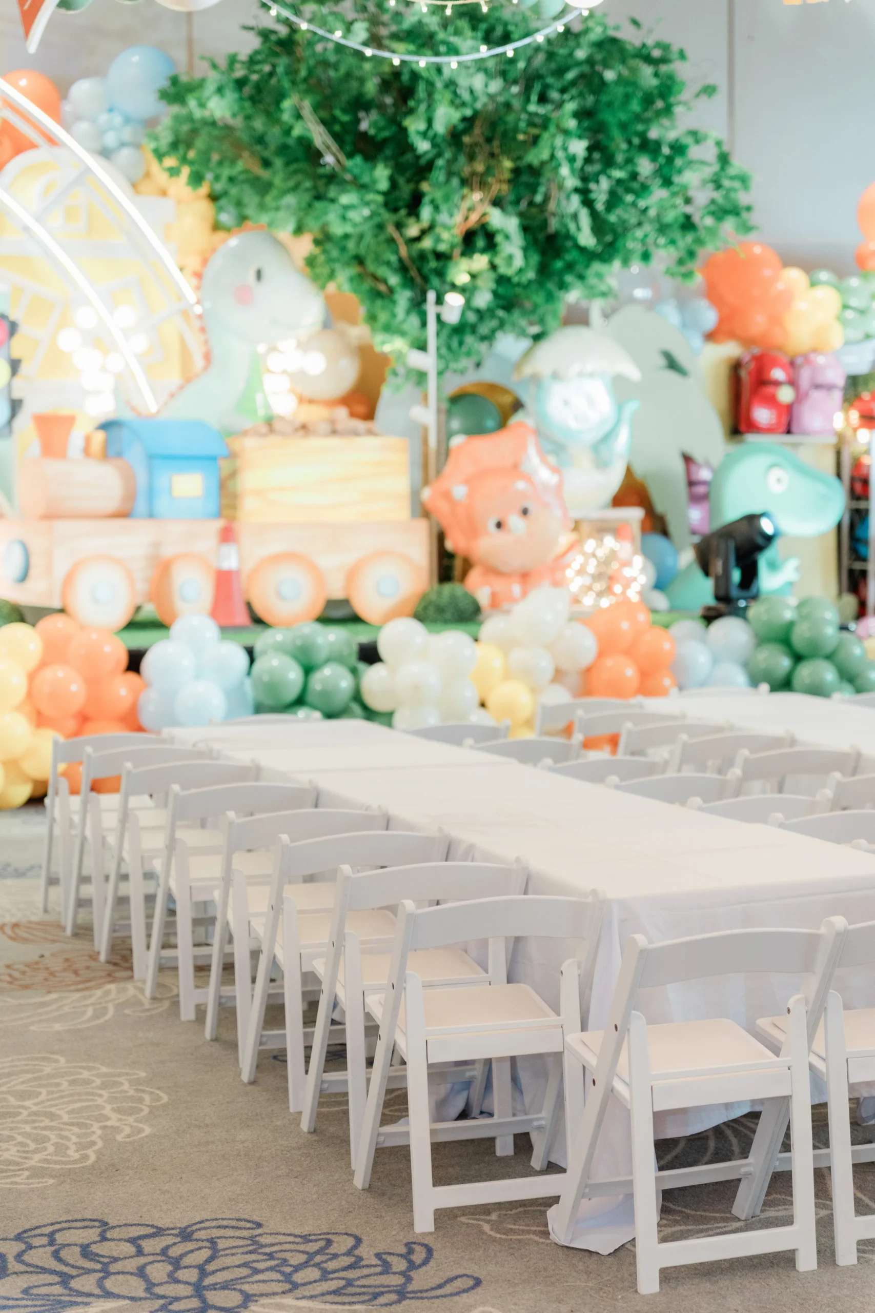 Pastel dinosaur birthday stage with balloons, trees and city decorations