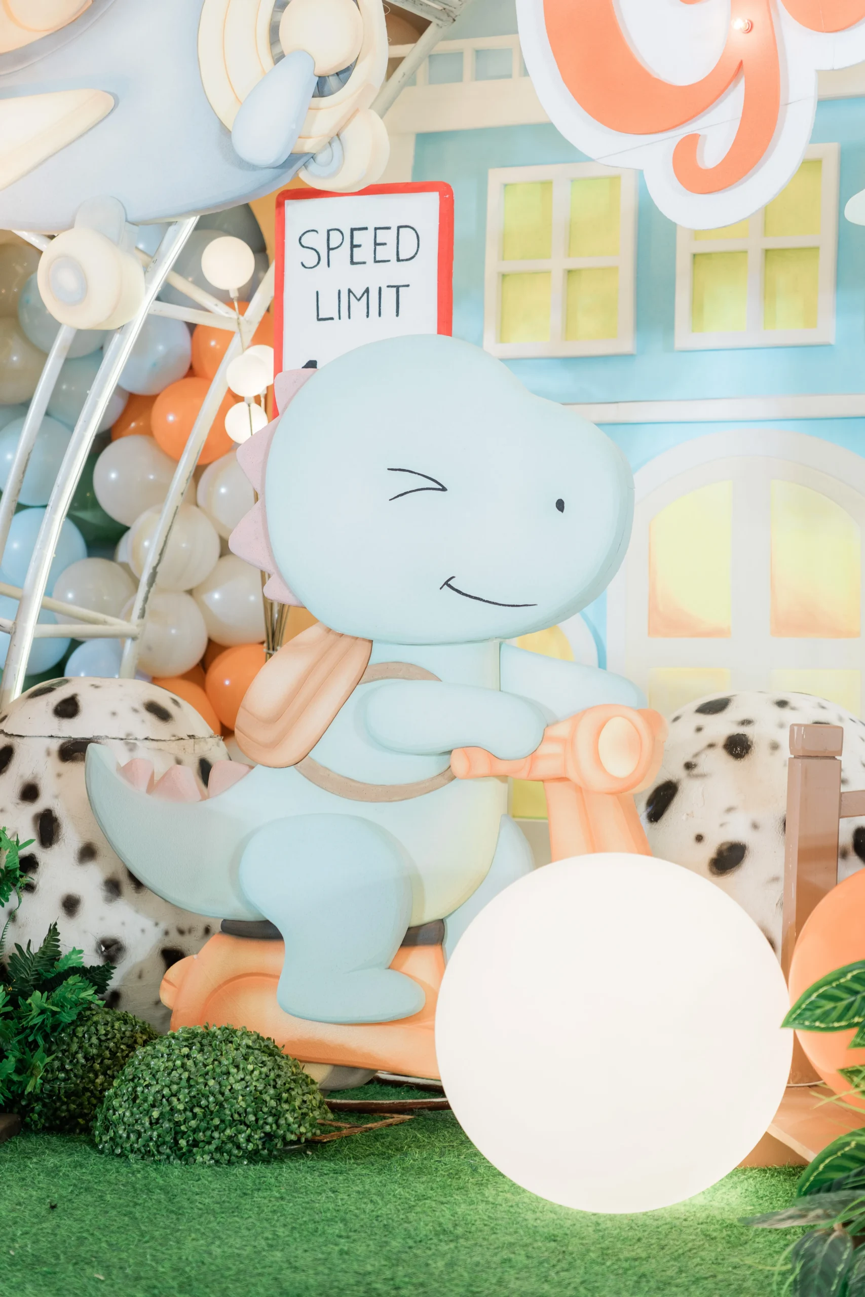Pastel dinosaur birthday stage with balloons, trees and city decorations