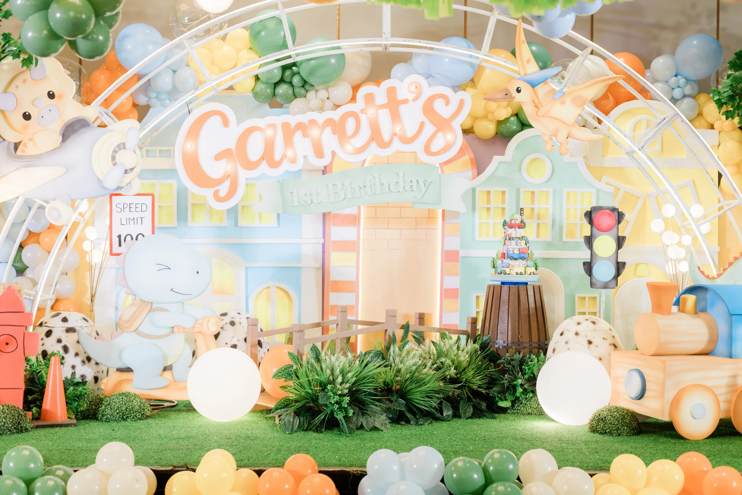 Pastel dinosaur birthday stage with balloons, trees and city decorations